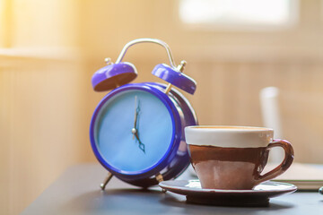 The alarm clock set by the window in the morning beside the coffee cup is used to set the time to remind appointments, is an analog alarm clock that sends alarms by tapping the side bell.