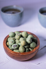 Wasabi snack in a wooden bowl with green tea in background. Vertical picture. Asian concept.