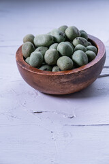 Spicy wasabi peanuts in a bowl on white textured background. Vertical picture.
