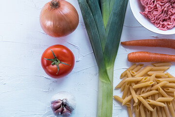 Minced meat, carrot, macaroni, leek, tomato, onion and garlic on white textured background. Italian pasta bolognesa. Top view.