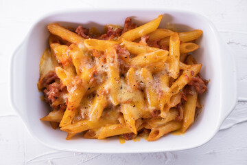 Pasta bolognesa in a baking dish with gratin cheese on white textured background. Italian cuisine. Top view.