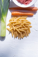 Macaroni with leek, carrot and meat to cook pasta sbolognesa on white background. Vertical picture.