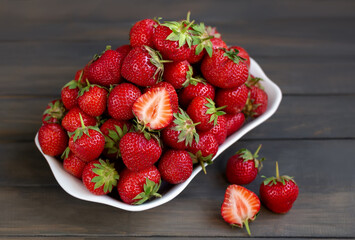 Bunch of fresh ripe strawberries in a white bowl on a dark wooden background 