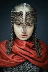 portrait of gorgeous young woman in  knight armour and steel chainmaille on dark background. Strong and sensual woman with perfect skin and with natural makeup.