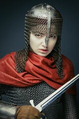 Gorgeous young woman in knight armour and steel chainmaille holding sword on dark background. Strong and sensual woman with perfect skin and with natural makeup.
