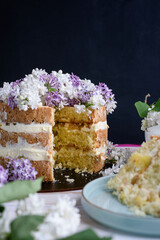 Biscuit cake with cream, impregnated with coconut and pineapple, decorated with lilac flowers.