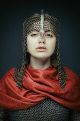 portrait of gorgeous young woman in  knight armour and steel chainmaille on dark background. Strong and sensual woman with perfect skin and with natural makeup.