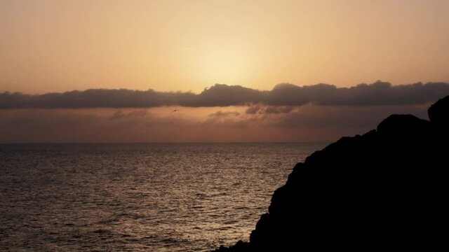 Sunset in the ocean in calm with lineal clouds in the horizont and a big rock