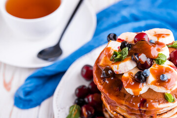 Delicious homemade pancakes with banana, berries, salted caramel, mint, tea.