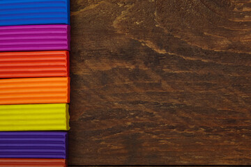 Multicolored smooth pieces of plasticine from the right on a brown wooden background with an empty space for the text