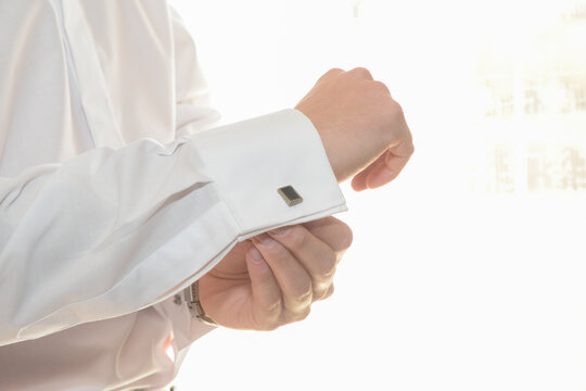 
Primer plano del brazo de un hombre que está poniendo un bonito gemelo en el puño de su camisa blanca con fondo en clave alta.