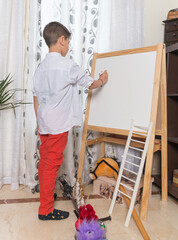 Niño pintando en una pizarra blanca en el interior de su casa durante la pandémia covid 19.