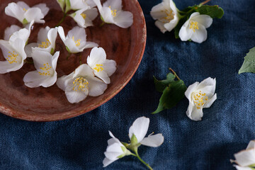 Obraz na płótnie Canvas White jasmine flowers, clay plate, on a dark blue textile background