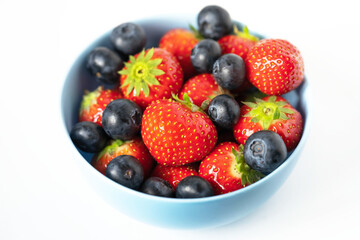 strawberries and blueberries in a blue bowl on a white background close up