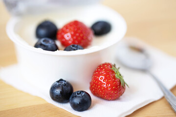 blueberries, strawberries, yogurt and a small spoon on a wooden table close-up