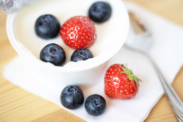 strawberries, blueberries, yogurt in a jar and a metal spoon on a wooden table