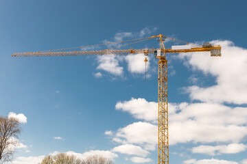 yellow hoist crane against a blue sky with clouds