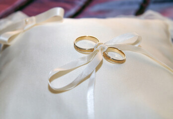 Dos anillos de oro y plata atados con un lazo a un pequeño cojín blanco. - obrazy, fototapety, plakaty
