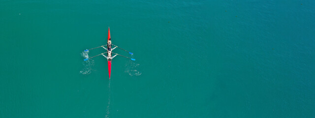 Aerial drone ultra wide photo of young women athletes rowing in canoe competition in tropical lake with emerald waters