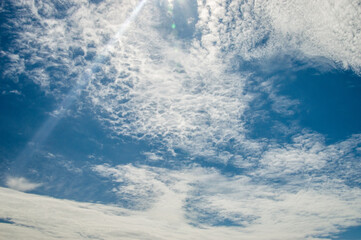 Patterned clouds in a deep blue sky with a lense flare