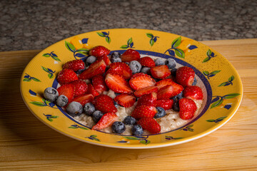 Oatmeal with fresh strawberries and frozen blueberries with cinnamon on a table in a plate