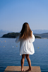 Young beautiful woman in white dress and sunglasses blowing soap bubbles on pier with seaview background. The concept of joy, ease and freedom during the vacation. The girl is enjoying the rest.