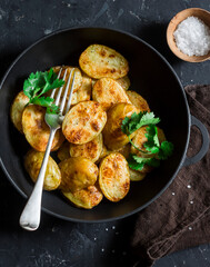 Roasted young potatoes in a cast iron skillet on a dark background, top view