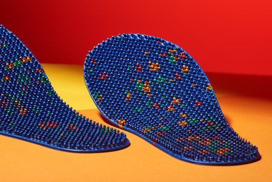 Blue massage insole for feet, with metal needles, spikes, on a yellow-orange background. For relaxation, health. Advertising, thematic and subject shooting.
