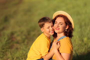 Cheerful young family: mother and little son hug and kiss each other in the sunset in summer