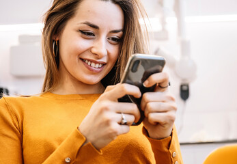Cheerful patient using smartphone in dental clinic