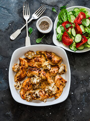 Roasted chicken fillet with cauliflower and fresh tomatoes, cucumbers salad on a dark background, top view