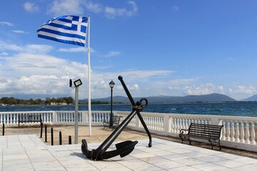 Greek flag behind a large old anchor at the sailors monument town square, in Preveza, Greece. View of Aktio and Ambracian gulf at the background