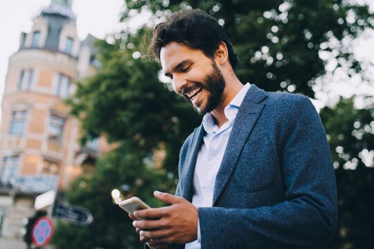 Cheerful man using smart phone while standing in city