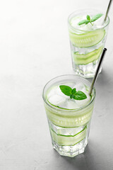 A refreshing cocktail with cucumber slices, mint leaves and ice cubes in glasses. Light gray concrete table. Vertical orientation with copy space.