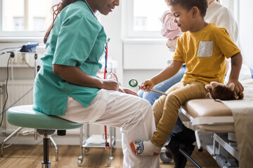 Midsection of pediatrician by boy with medical equipment in clinic
