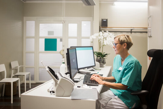 Side view of mature female doctor working over computer while sitting in clinic