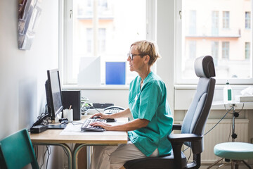 Side view of mature female doctor working over computer while sitting in clinic