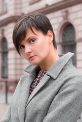 Autumn fashion outdoor. The brunette girl with short hair in fashionable stylish grey coat, posing on the background of building. Street fashion.Autumnal lifestyle