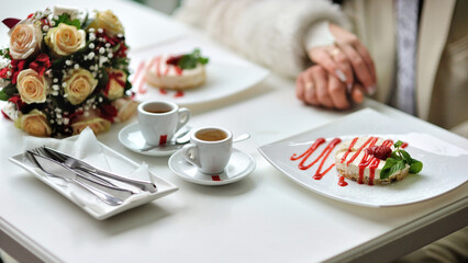 The newlyweds are sitting holding hands in a beautiful cafe with a cup of coffee, a delicious dessert, a wedding bouquet on the table and various accessories. Photography, concept.