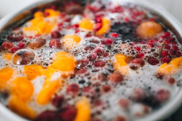 Fresh fruits are boiled in boiling water in a metal pan on a stove with bubbles and foam close-up. Cooking a delicious compote of apricot, apples, cherries, raspberries. Photography, concept.