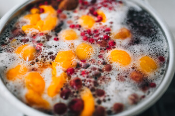 Fresh fruits are boiled in boiling water in a metal pan on a stove with bubbles and foam close-up. Cooking a delicious compote of apricot, apples, cherries, raspberries. Photography, concept.