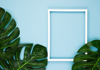 Creative layout of tropical exotic leaves with a white empty frame on a soft blue background. The concept of summer nature