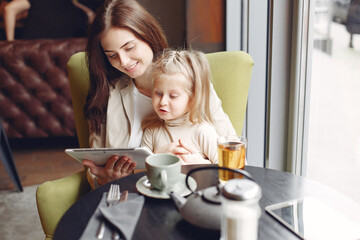 Mother with daughter. Family in a cafe. Woman use the tablet.