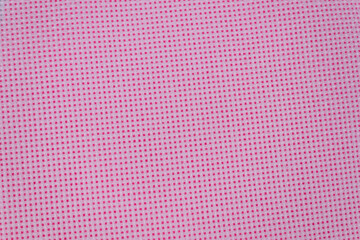 on a pink background, highlighted in close-up, a piece of dense fabric with holes for embroidery with threads, pink.