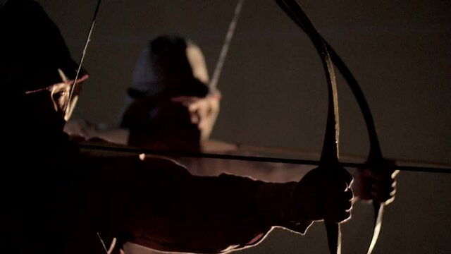 Two men are shooting arrows in a dark room. Archery. Historical Archery