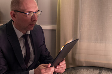 A businessman reads hot noses on a tablet. The tablet burns in a bright flame.