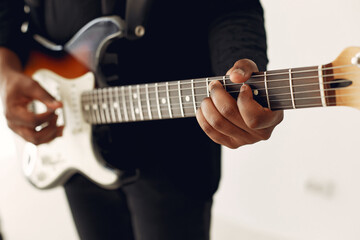 Obraz na płótnie Canvas Black man in a studio. Guy in a black suit. Musician with a guitar.