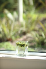 glass of water with green grass in front of a window 