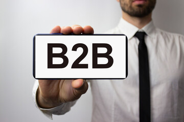 The inscription b2b on the phone held by a young businessman in his hand. Business concept between...