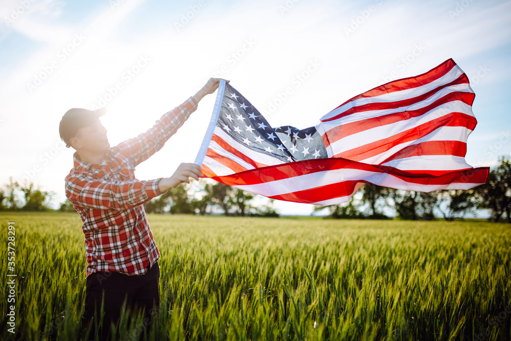 Wall mural young patriotic farmer stands among new harvest. boy walking with the american flag on the green whe